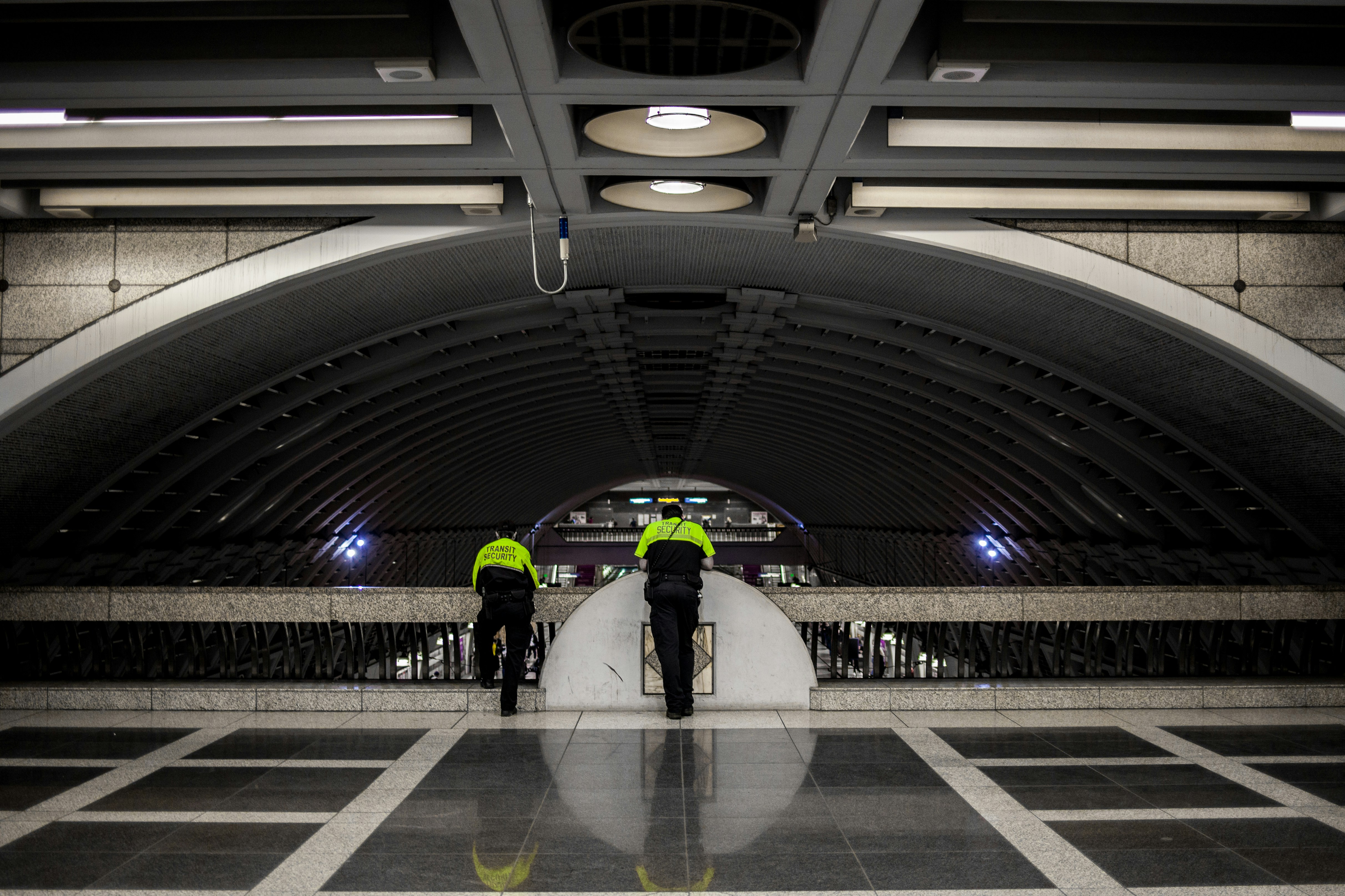landscape photography of two men leaning on barricade, Two security guards overlooking pioneer square light rail station.