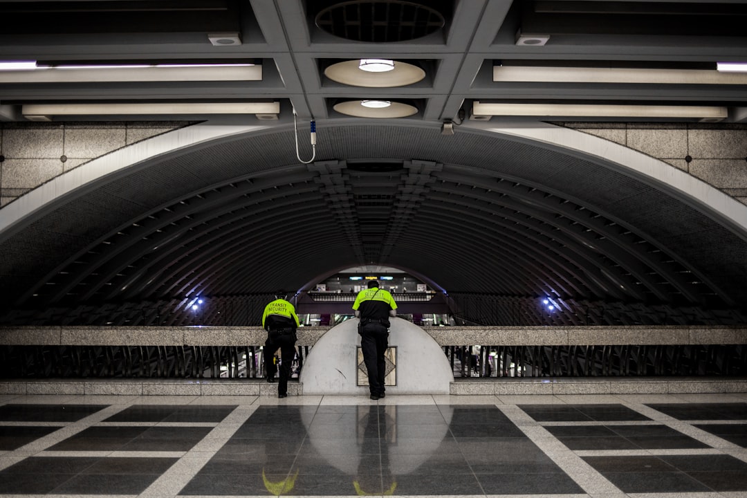 landscape photography of two men leaning on barricade, Two security guards overlooking pioneer square light rail station