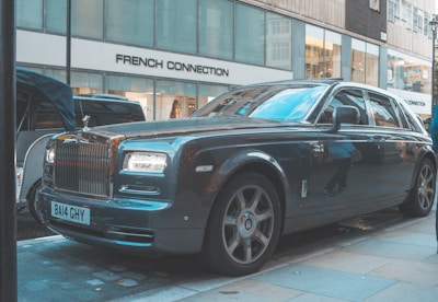 A sleek, luxury car is parked on a city street in front of a store called French Connection, with large windows reflecting the urban environment. The car is shiny and appears to be well-maintained, adding an air of sophistication and wealth to the scene.