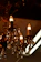 An ornate chandelier with multiple candle-like light bulbs is adorned with hanging crystal pendants. The chandelier exhibits intricate metalwork with decorative elements and a warm, amber glow from the bulbs and crystals.