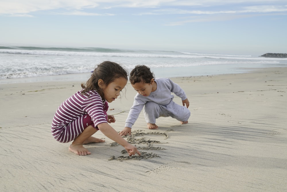 two kids playing and writing on sand near shore