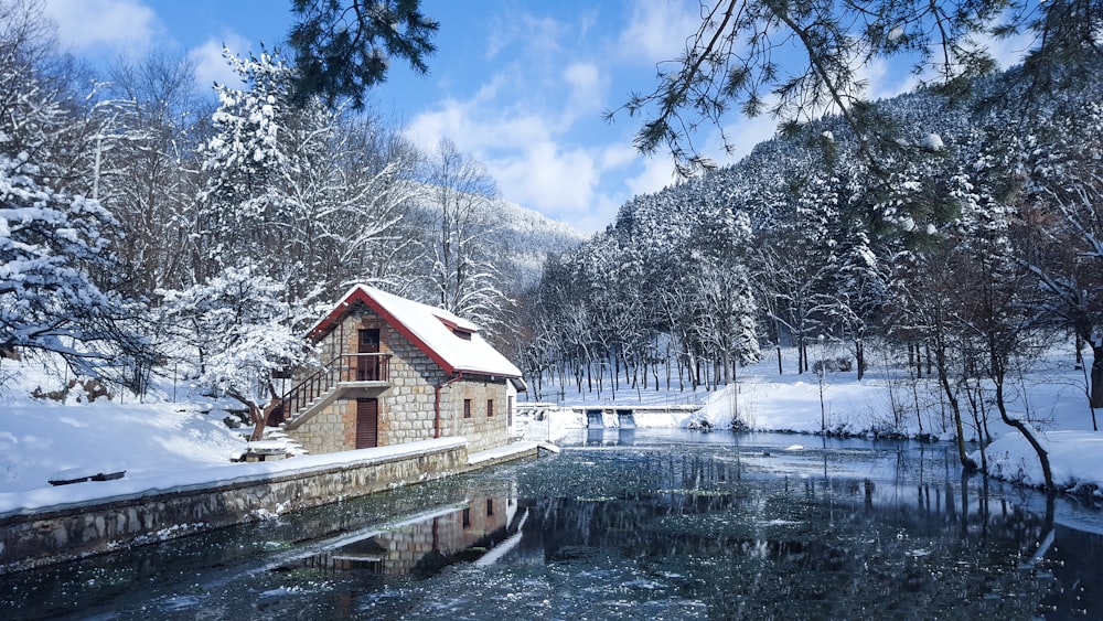 white and red house near river with snow covered field during daytime