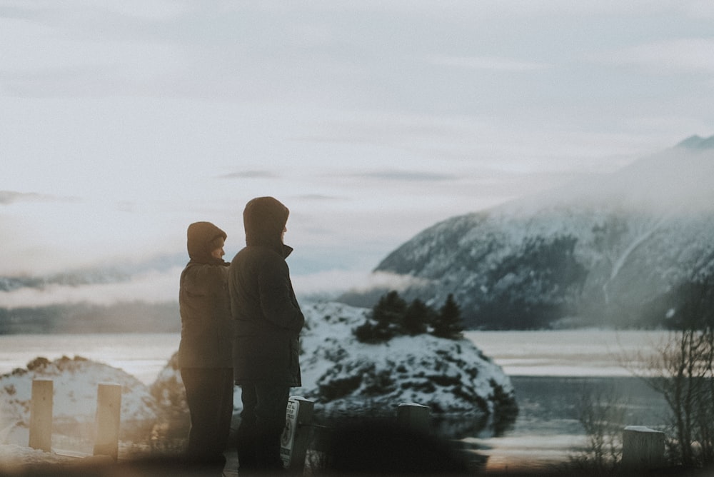 two person standing near body of water under foggy weather during daytime