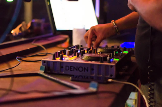 Close-up of DJ hands adjusting mixer knobs under red and black club lighting.