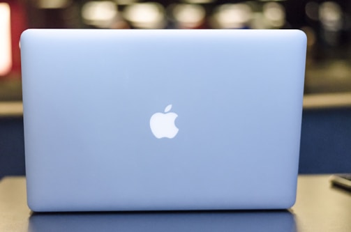 A sleek, silver laptop displaying a prominent glowing apple logo on its lid, set against a blurred background with soft lighting.