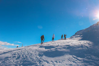A diverse group of hikers preparing their gear amid snowy mountain terrain under a clear blue sky.