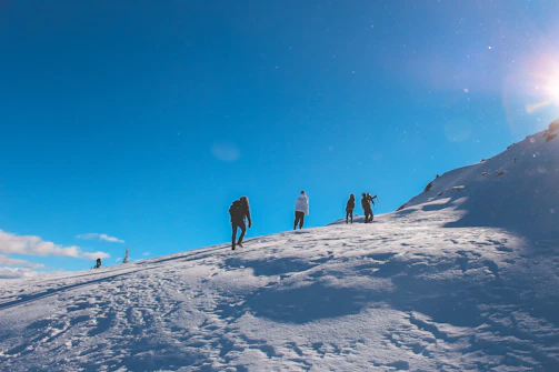 A diverse group of hikers preparing their gear amid snowy mountain terrain under a clear blue sky.