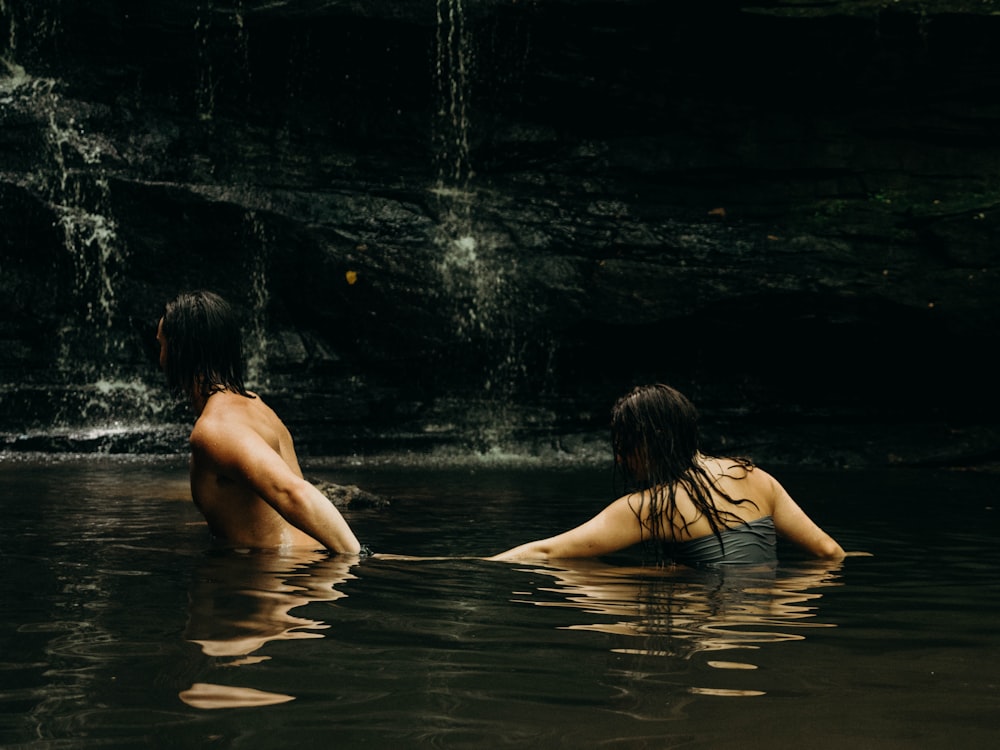 woman behind man on body of water near gray rocks