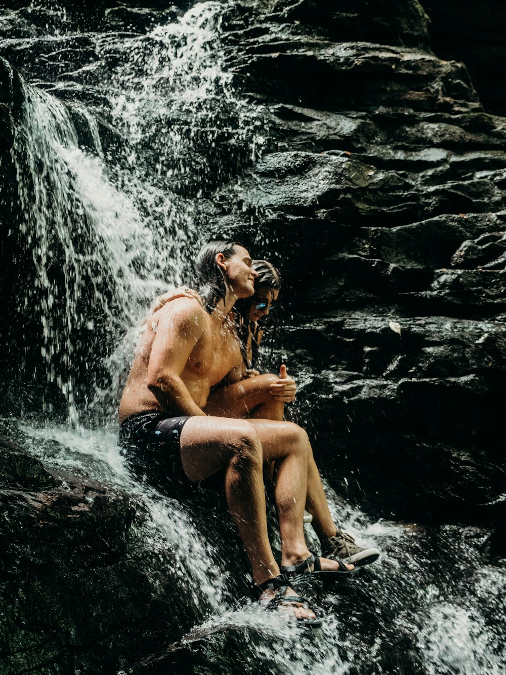 woman and man sitting on the waterfalls rock