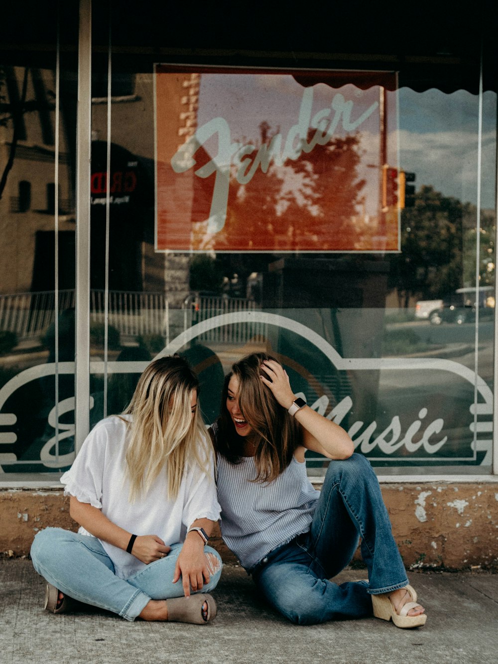 dos mujeres riendo sentadas frente a la tienda Fender