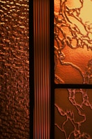 An intricate design of textured glass panels showcasing a combination of patterns and textures. The glass on the left features a wavy, textured surface that resembles rippling water, while the section on the right has an organic, vine-like pattern with a cracked surface. The central panel is a vertical strip with a linear, ribbed texture.