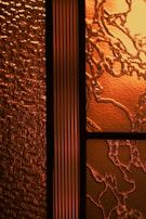 An intricate design of textured glass panels showcasing a combination of patterns and textures. The glass on the left features a wavy, textured surface that resembles rippling water, while the section on the right has an organic, vine-like pattern with a cracked surface. The central panel is a vertical strip with a linear, ribbed texture.
