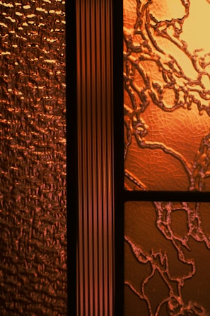 An intricate design of textured glass panels showcasing a combination of patterns and textures. The glass on the left features a wavy, textured surface that resembles rippling water, while the section on the right has an organic, vine-like pattern with a cracked surface. The central panel is a vertical strip with a linear, ribbed texture.