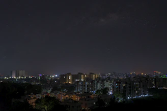 City skyline at night with glowing lights and starry sky.
