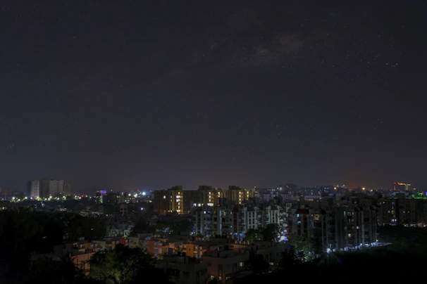 City skyline at night with glowing lights and starry sky.