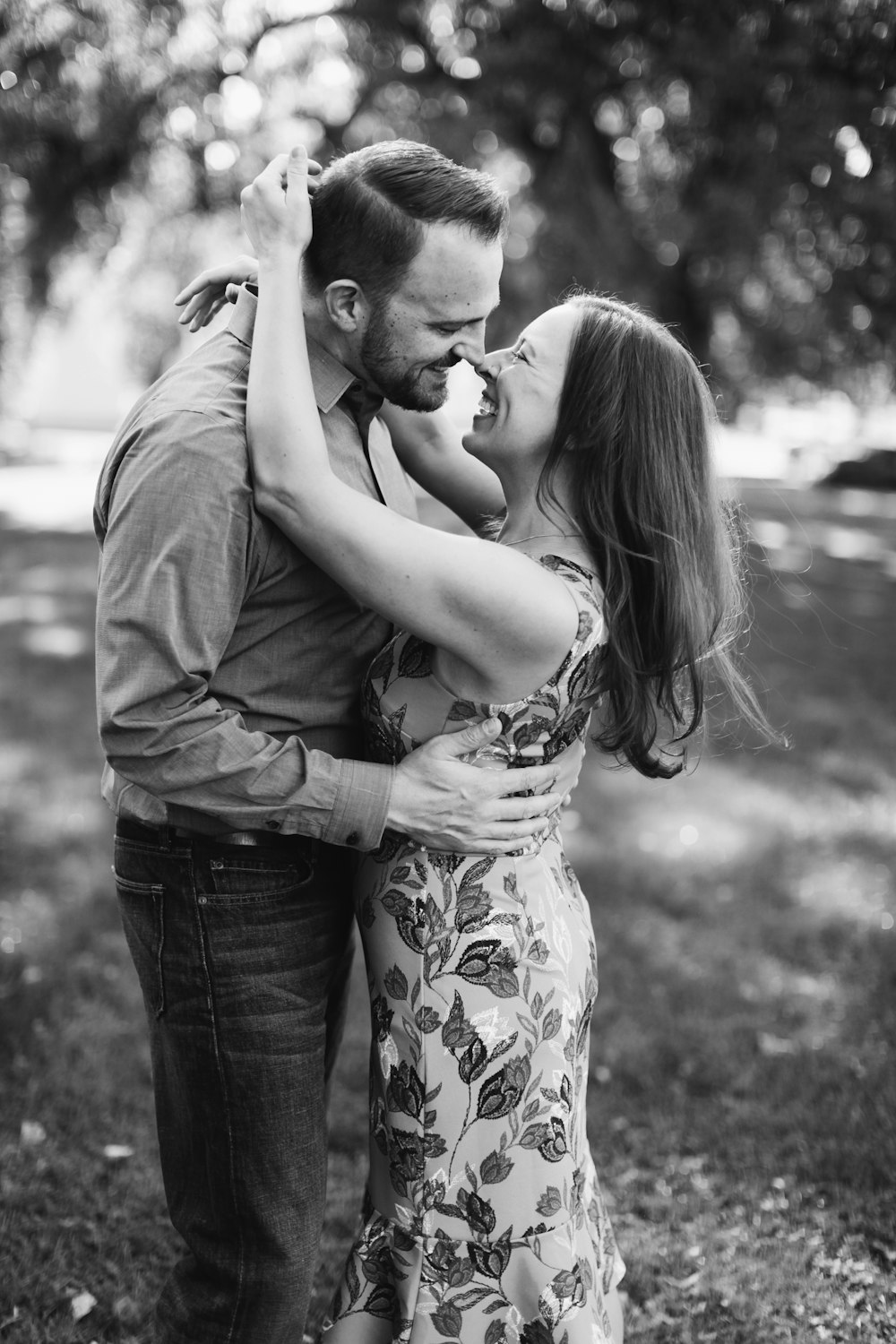 grayscale photography of smiling couple standing beside trees
