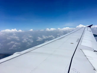 A cozy airplane cabin seat with a window view showing fluffy clouds and blue sky.