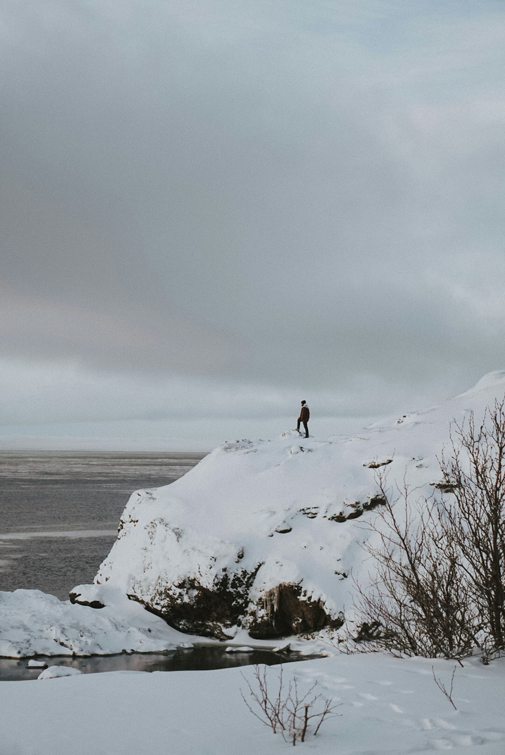 海に面した雪に覆われた山の崖の上に立つ男