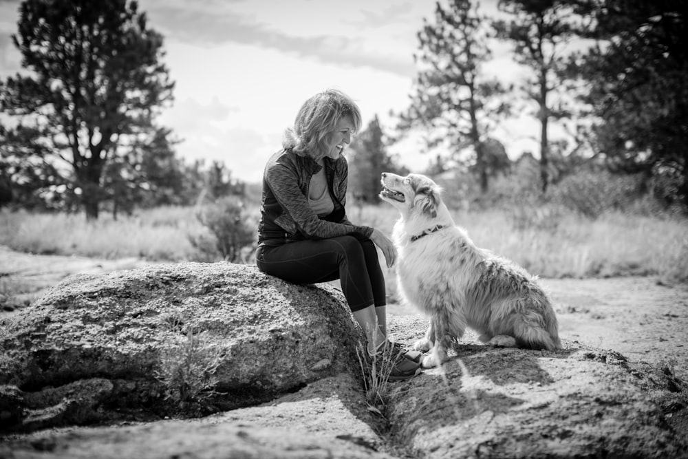 Frau sitzt mit Hund auf Felsen