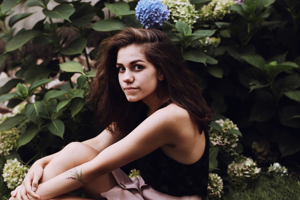 woman in black sleeveless top sitting on ground near plants