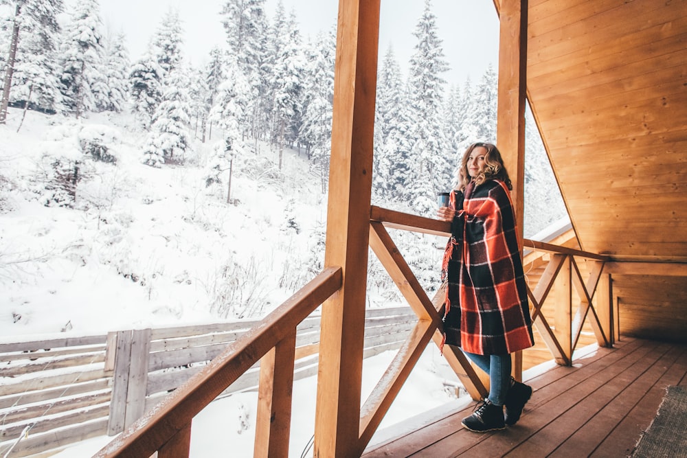 woman standing on wooden deck while wrapped with red and black blanket