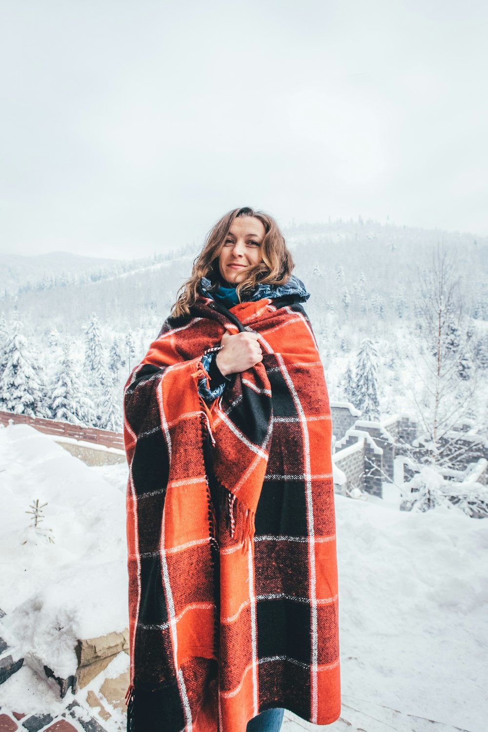 woman covered with red and black checked blanket surrounded by snow
