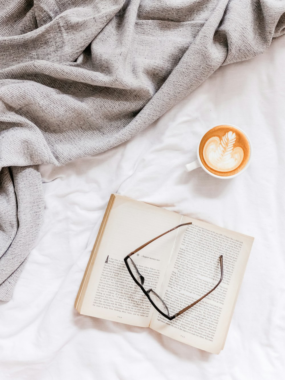 flat lay photography of eyeglasses on top of open book beside cup of coffee late