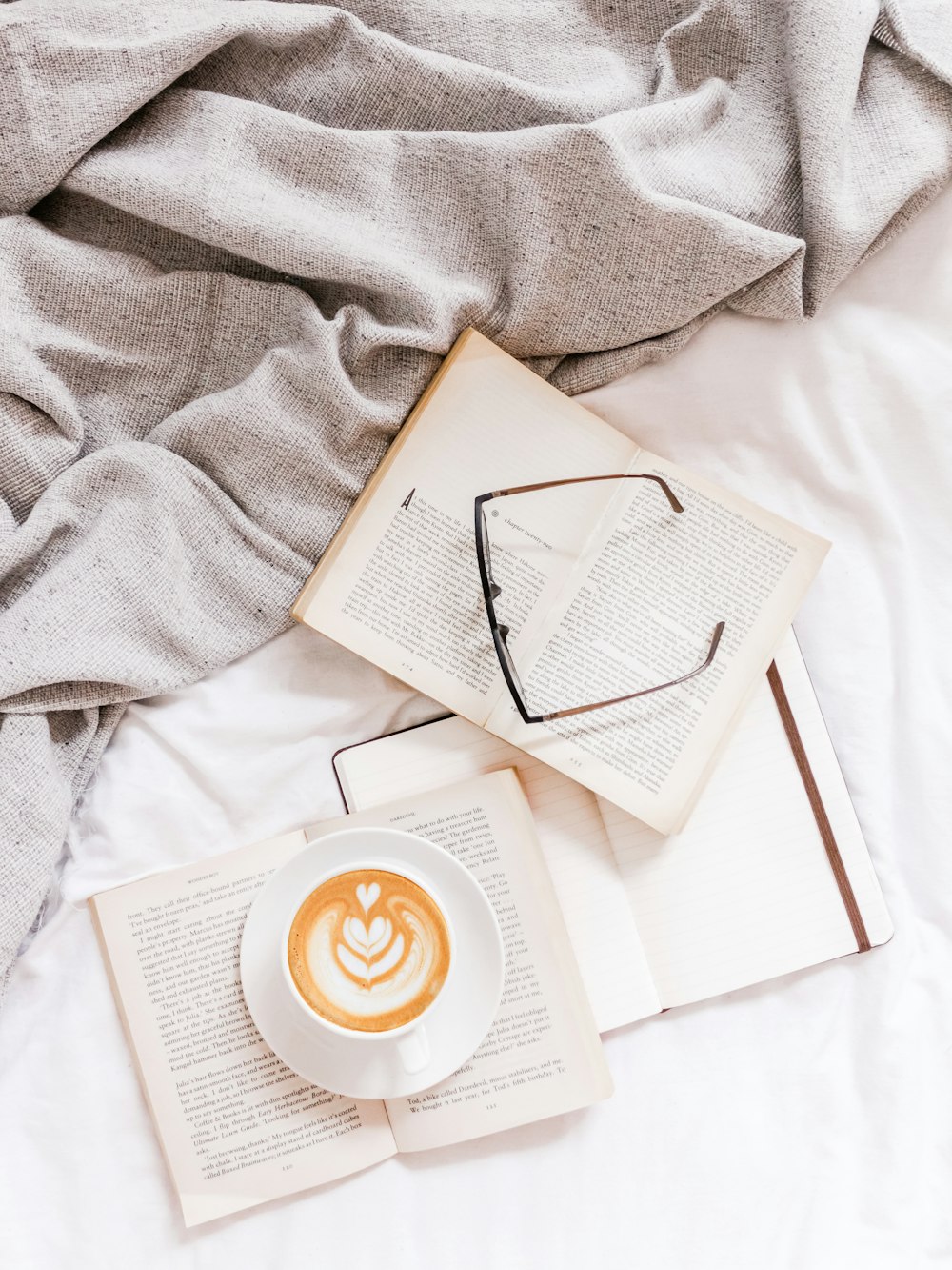 three opened books and eyeglasses on white textile