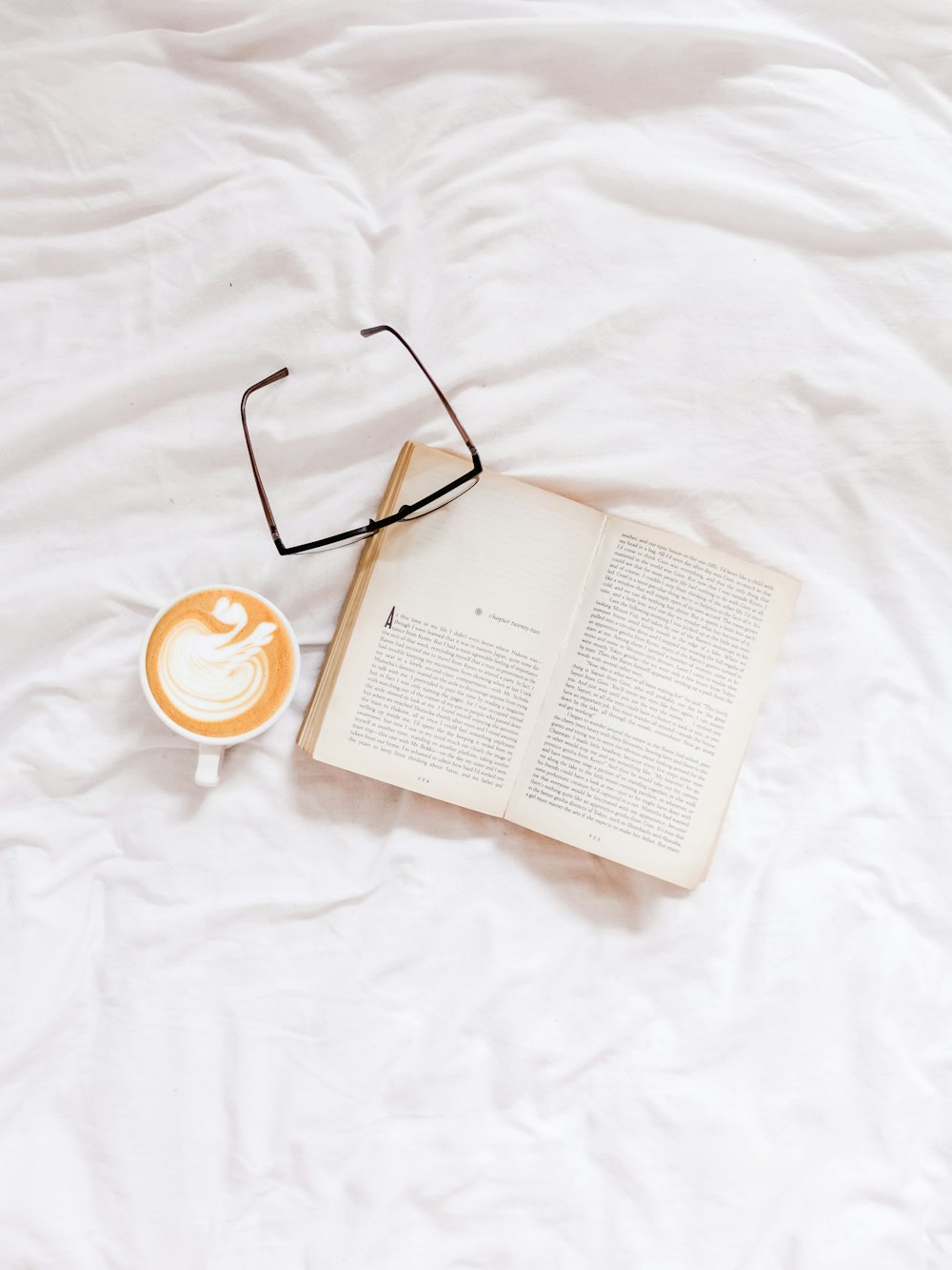 opened book and eyeglasses on white textile