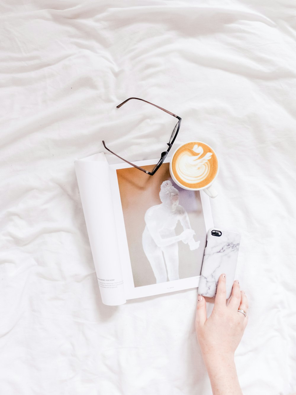 black framed eyeglasses, phone, and magazine on white textie