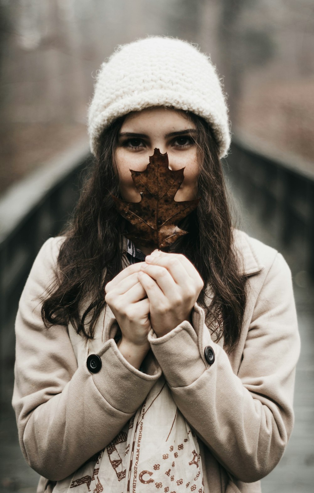 woman wearing coat and beanie hat holding dried leaf