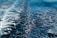A dynamic, swirling pattern of foam on a deep blue ocean surface, created by the wake of a moving boat. The contrast between the bright white foam and the dark blue water highlights the motion and texture of the sea.