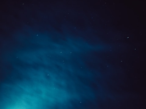 A night sky filled with scattered stars and wispy clouds, creating a deep, tranquil atmosphere. A subtle gradient of dark blue to teal is present, giving a serene, cosmic feeling.