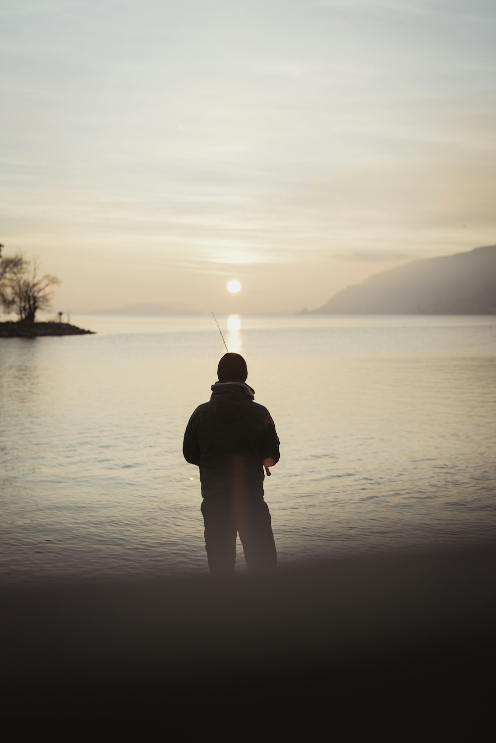 silhouette of person holding fishing rod across body of water