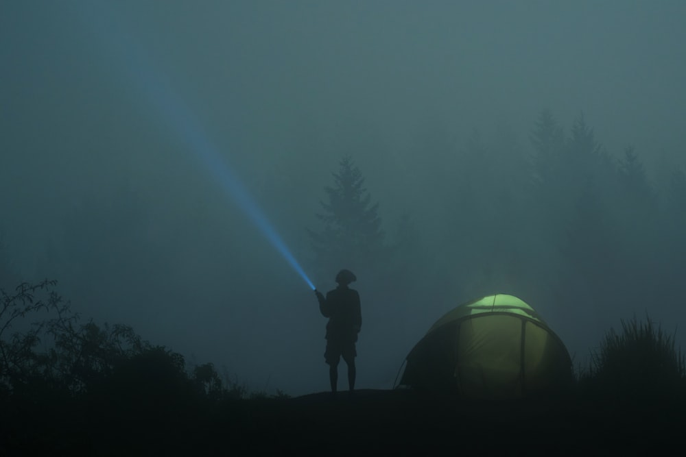 person standing near dome tent while holding flashlight