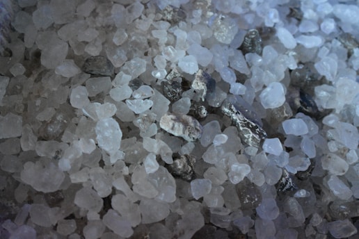 A close-up of pink Himalayan salt crystals scattered on a wooden surface, highlighting their natural hue and texture.