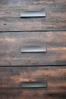 A close-up view of three wooden drawers with metallic handles, showing the grain and texture of the wood.