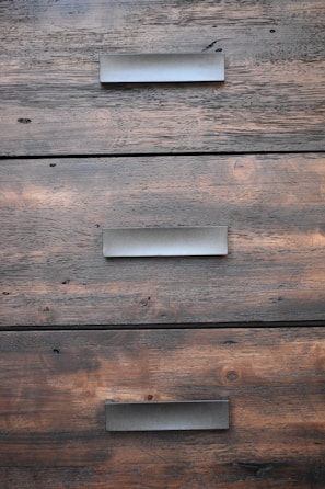 A close-up view of three wooden drawers with metallic handles, showing the grain and texture of the wood.