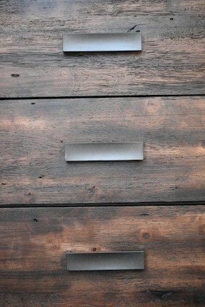 A close-up view of three wooden drawers with metallic handles, showing the grain and texture of the wood.