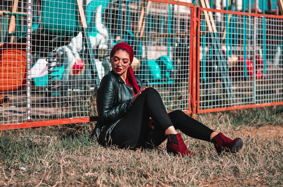 woman sits on green at the back of link fence