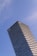 A tall modern skyscraper with a distinctive tiered design, featuring glass and steel architecture, set against a clear blue sky. The building displays a prominent corporate logo at the top.