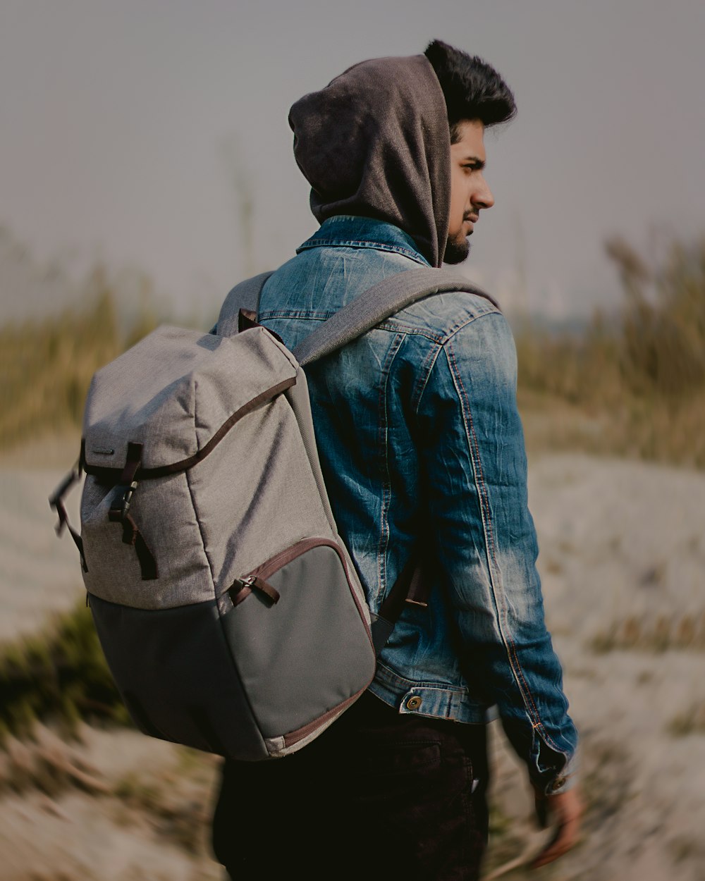 man with gray backpack facing trees while looking sideways at daytime in selective focus photography