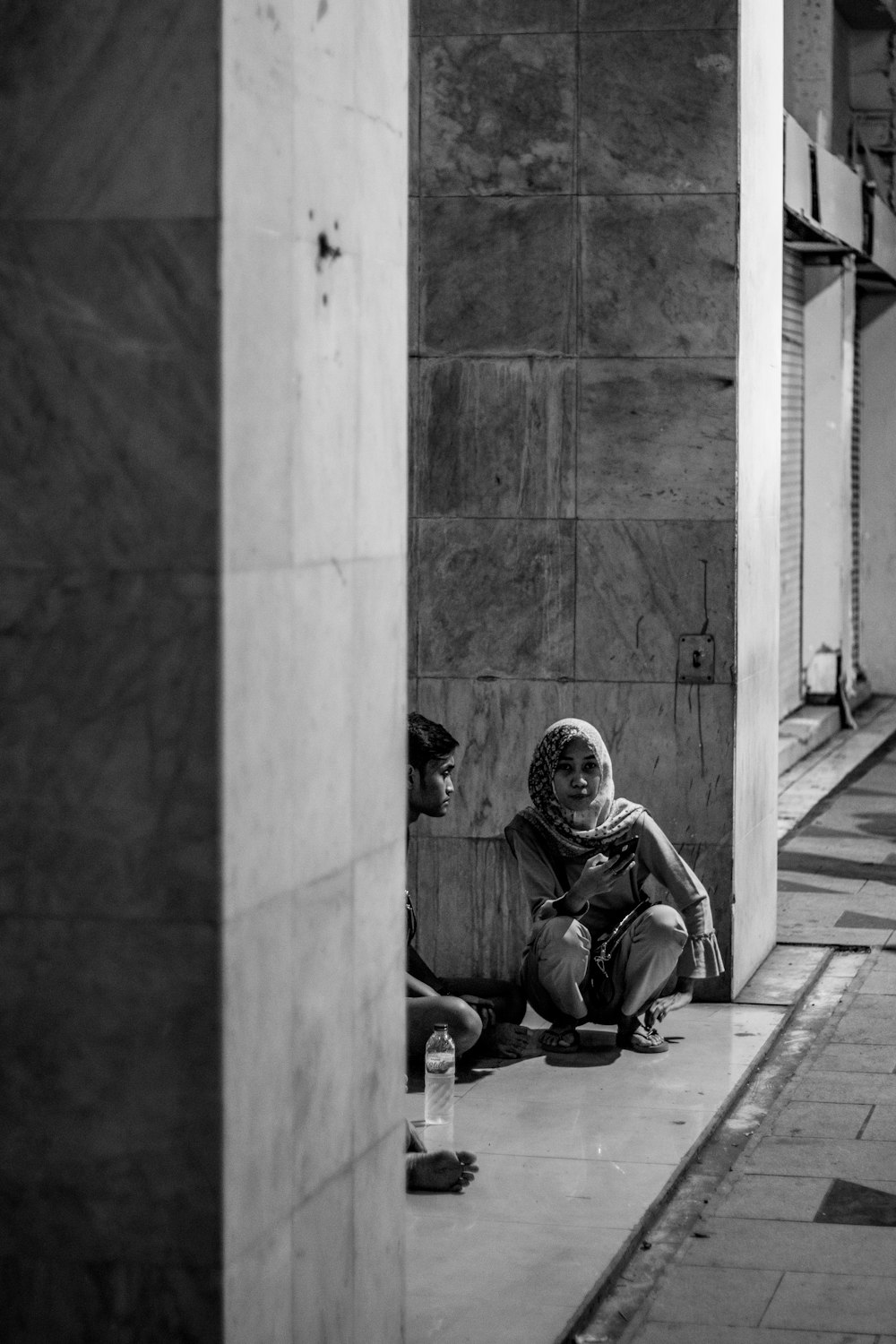 grayscale photo of woman sitting on gray surface