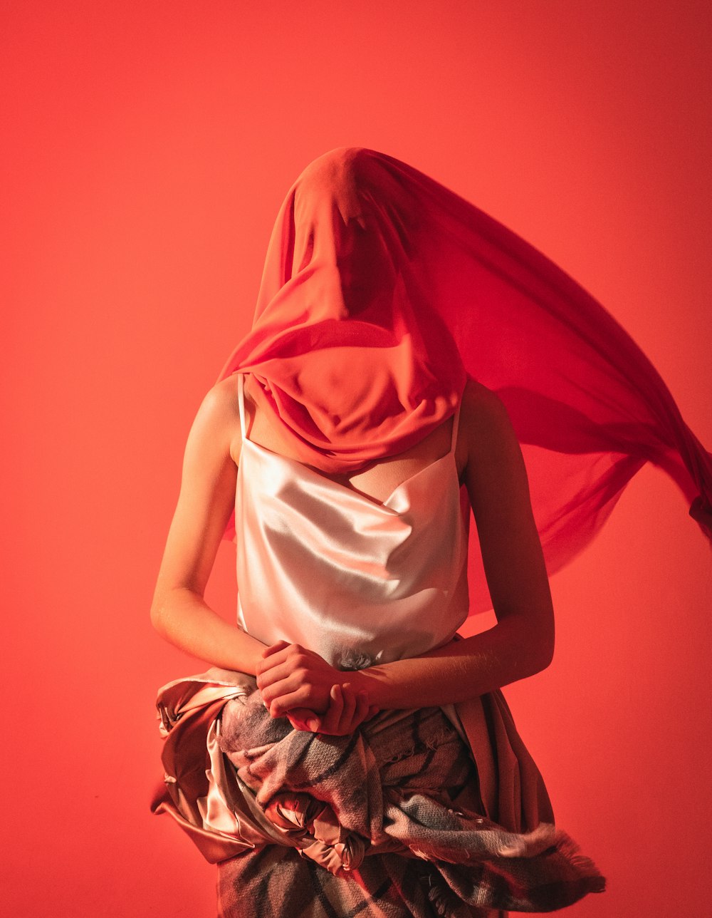 donna con canotta di seta bianca che copre il viso con un panno rosso