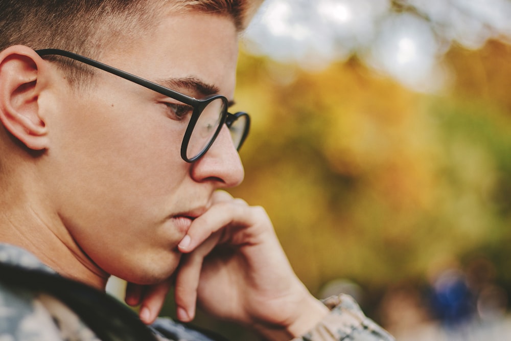 boy with black framed eyeglasses holding face