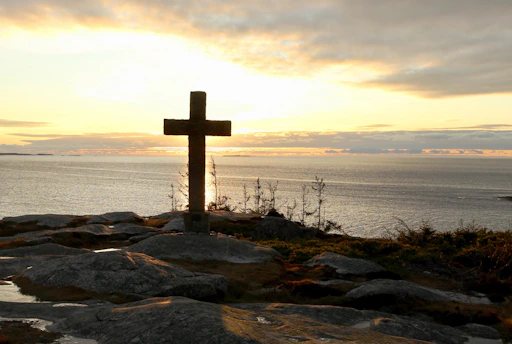 A serene sunrise behind an ancient stone cross standing on a hill, symbolizing reflection and inquiry.