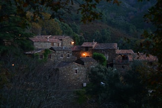 Cozy countryside guesthouse with warm lights glowing at dusk, surrounded by gentle hills.