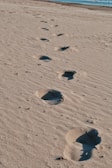 Woman walking along the shoreline, footprints trailing in the wet sand.