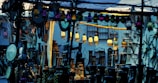 A marketplace stall displaying an array of decorative lanterns, mirrors, and vases. The scene is crowded with various ornamented items, with hanging colored lanterns illuminating the area in warm and cool tones. There are intricate designs and patterns evident in the items, creating an eclectic and vibrant atmosphere.