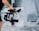 A person holds a professional camera mounted on a stabilizing rig, standing in a space with plastic sheeting covering furniture in the background.